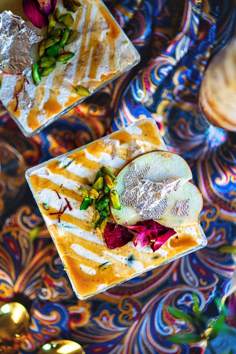 Layered Caramel Apple Shrikhand dessert topped with caramel drizzle, pistachios, apple slices, rose petals, and silver leaf for Diwali.