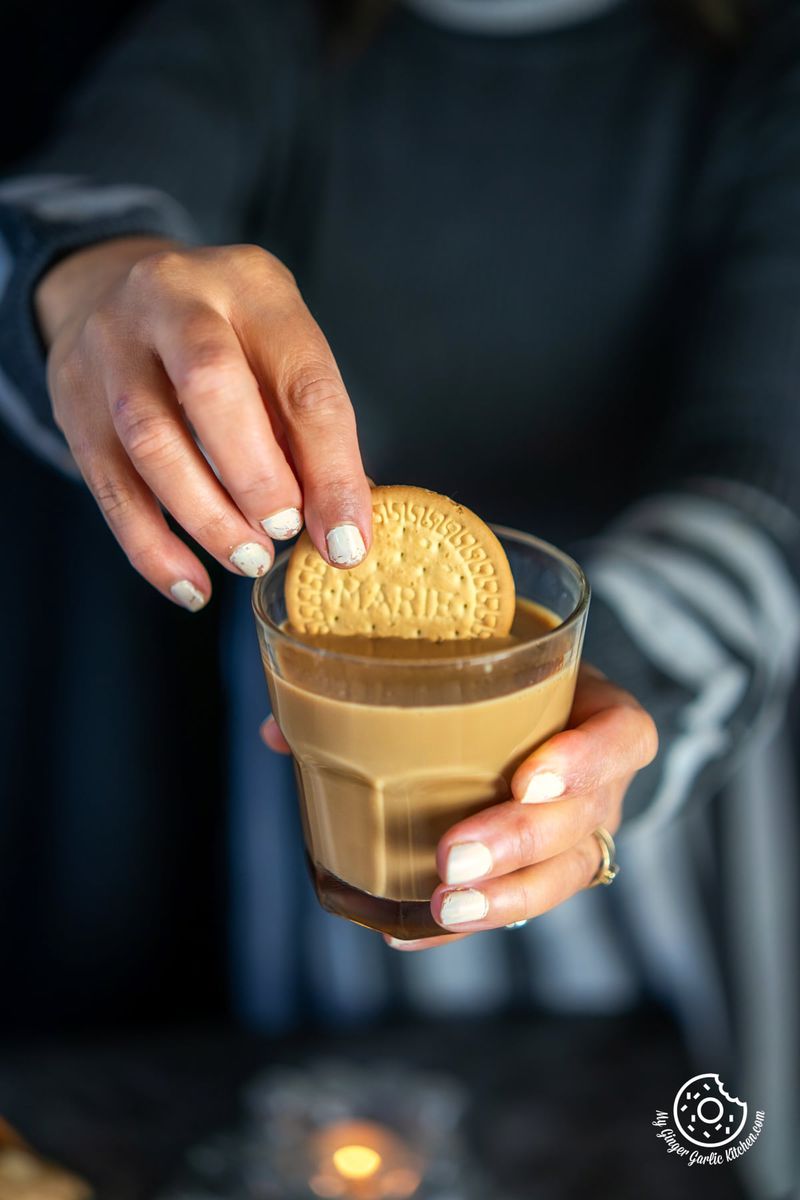 a person holding a cookie into a glass of caramel chai
