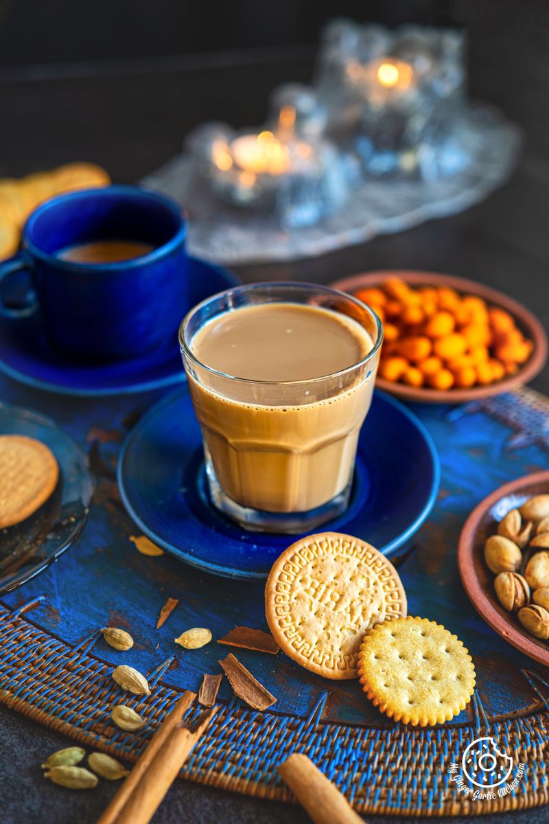 a transparent glass of caramel chai with cookies and crackers on a blue table
