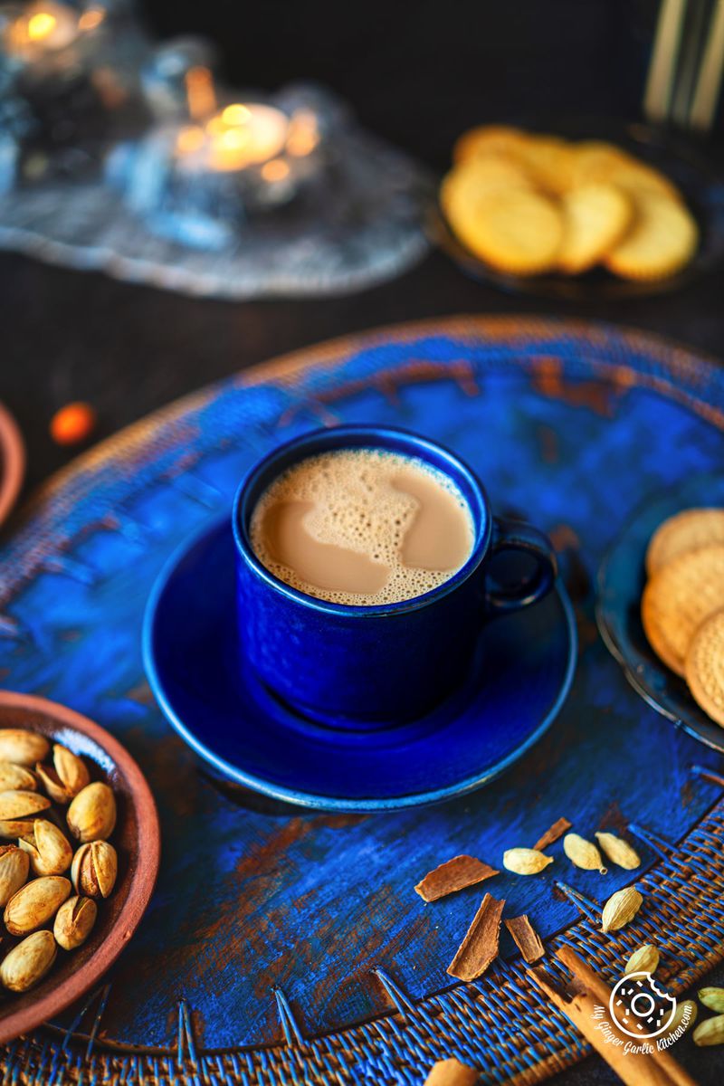 a cup of caramel masala chai with nuts and cookies on a blue table