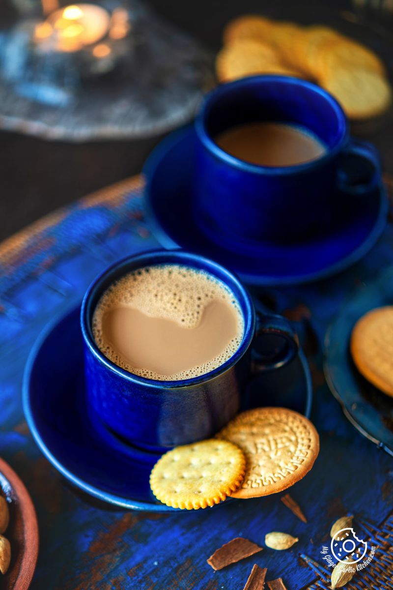 two cups of caramel masala tea and biscuits on a blue table