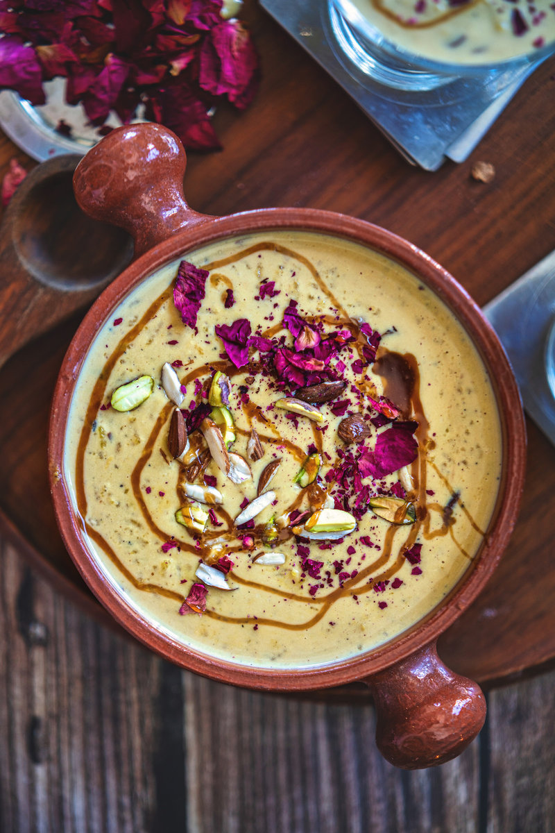 Caramel kheer in a traditional clay pot garnished with chopped nuts and dried rose petals.