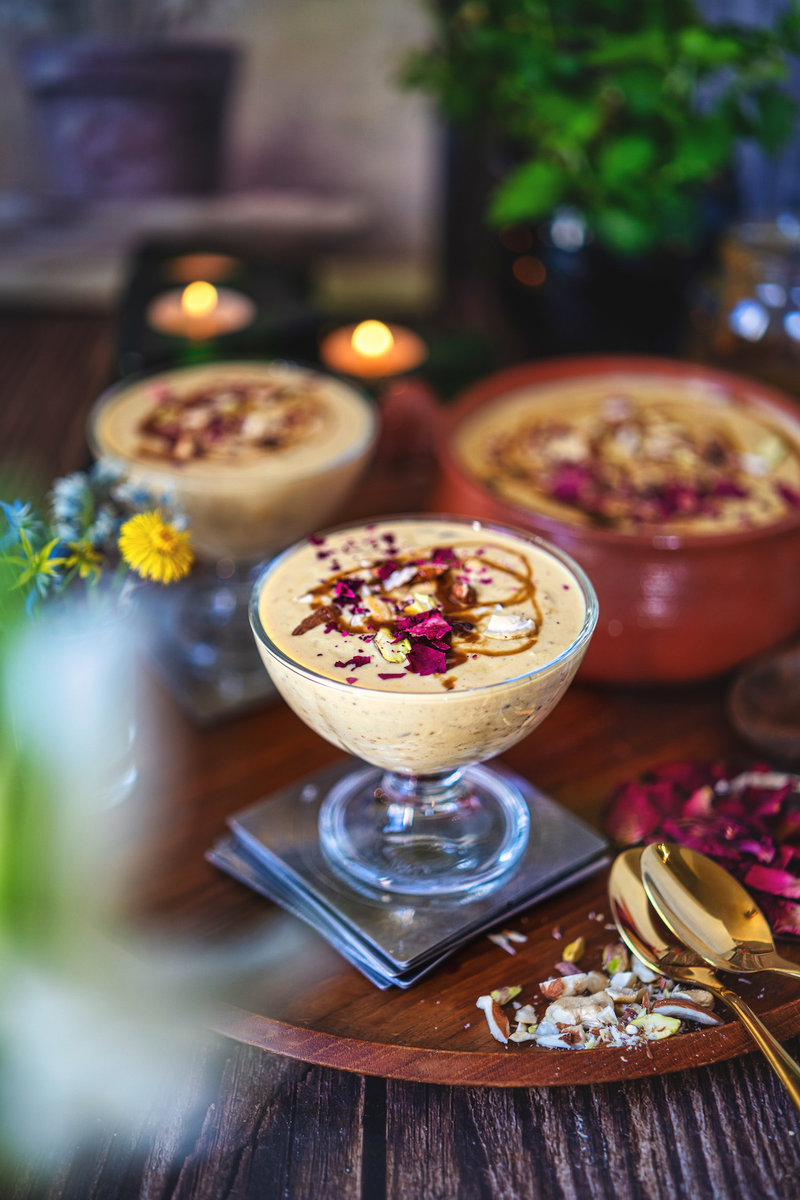 Elegant presentation of caramel kheer in a glass dessert bowl, topped with nuts and rose petals.