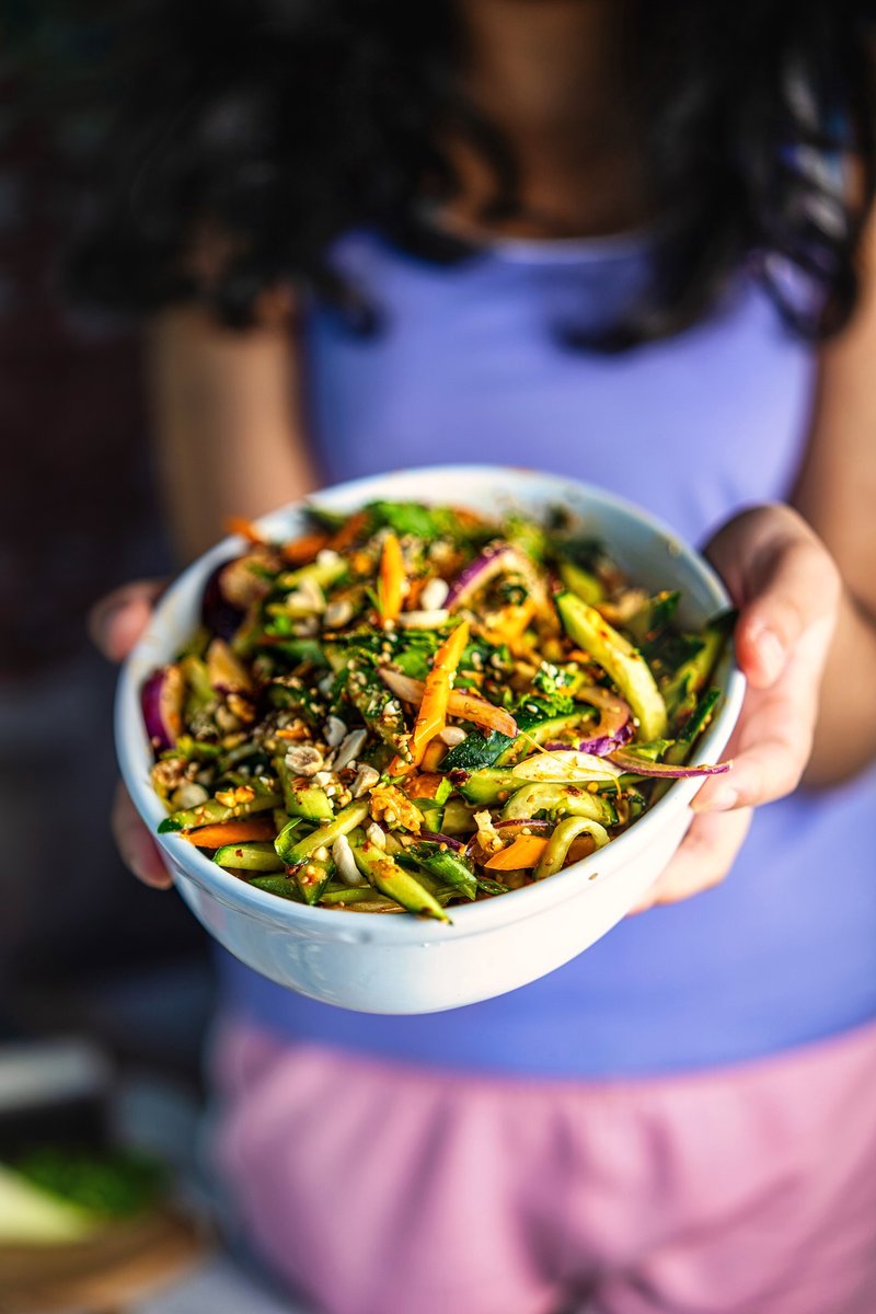 Asian cucumber carrot salad with roasted peanuts, sesame seeds, cilantro, and chili crisp served in a white bowl