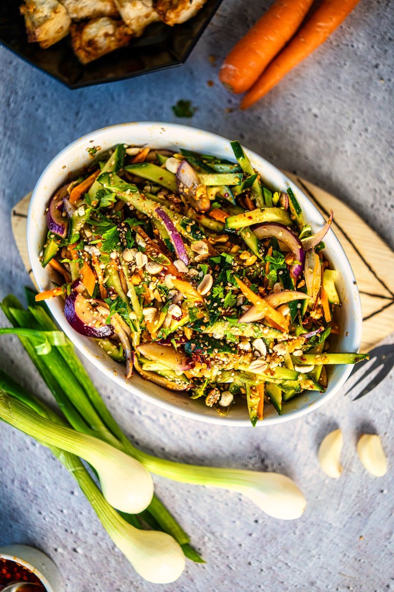 Carrot cucumber salad with roasted peanuts, toasted sesame seeds, red onion, and fresh cilantro served in a bowl
