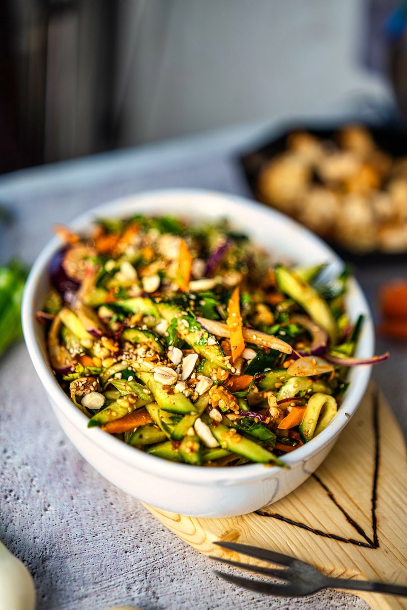 Crispy carrot cucumber salad with chili crisp, roasted peanuts, sesame seeds, and fresh herbs in a white serving bowl