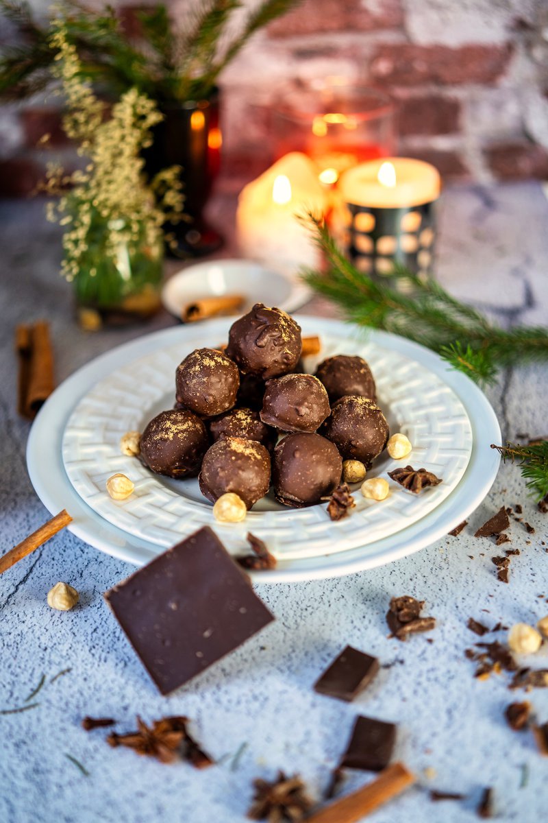 A plate of chai truffles with a stack of broken chocolate bars and loose pieces of chocolate and spices scattered on the table.