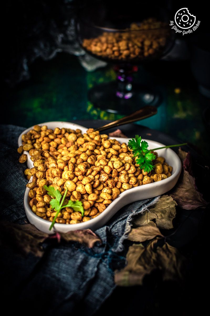 there is a bowl of chana dal namkeen on a table with a spoon and fresh cilantro 