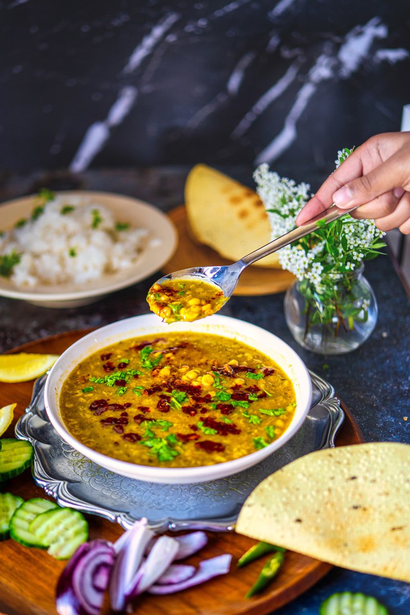 A spoonful of chana dal being lifted from a bowl, showcasing the thick and creamy texture, with rice and papad in the background.