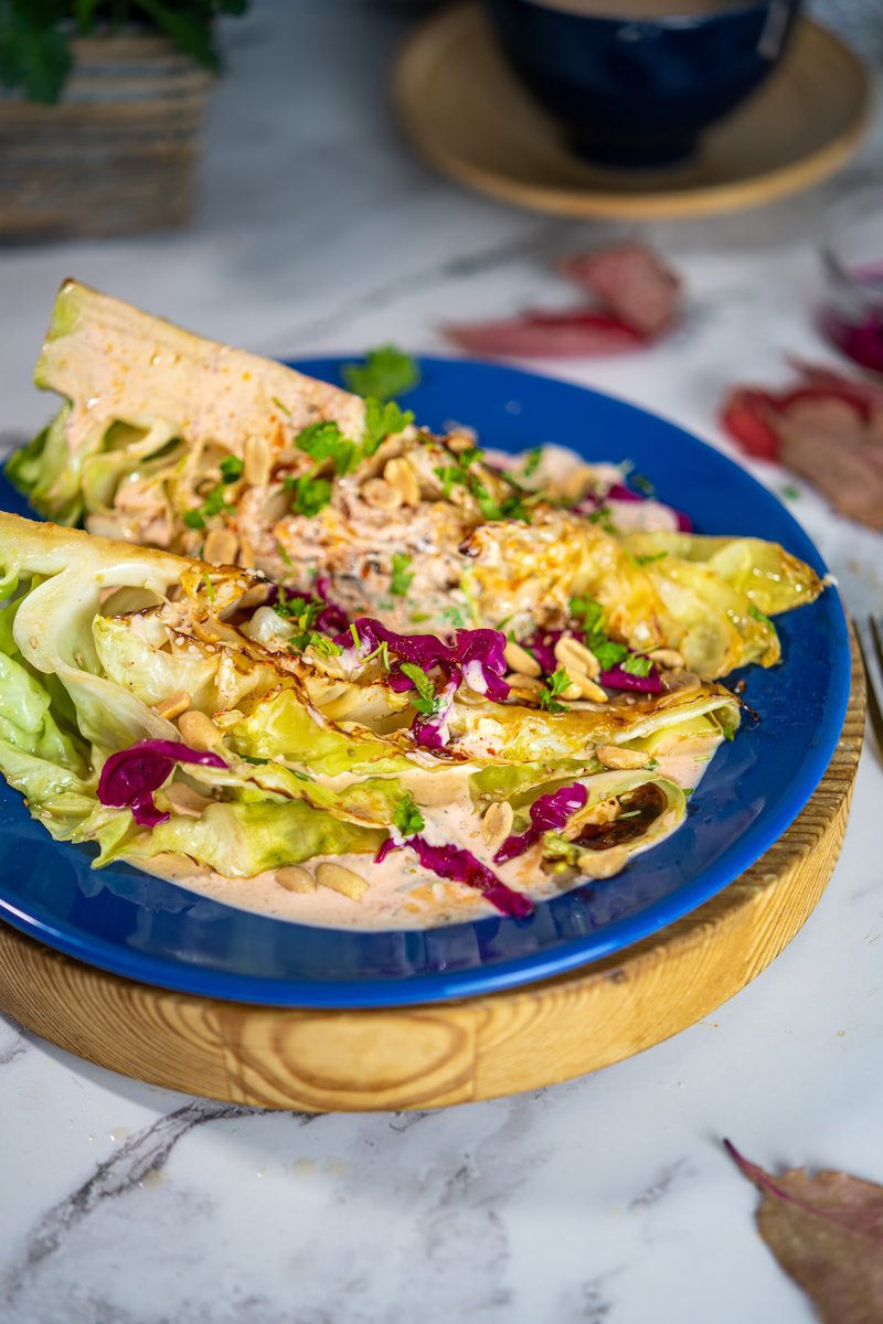 Grilled cabbage wedges with creamy sauce, roasted peanuts, purple cabbage and fresh herbs served on blue plate