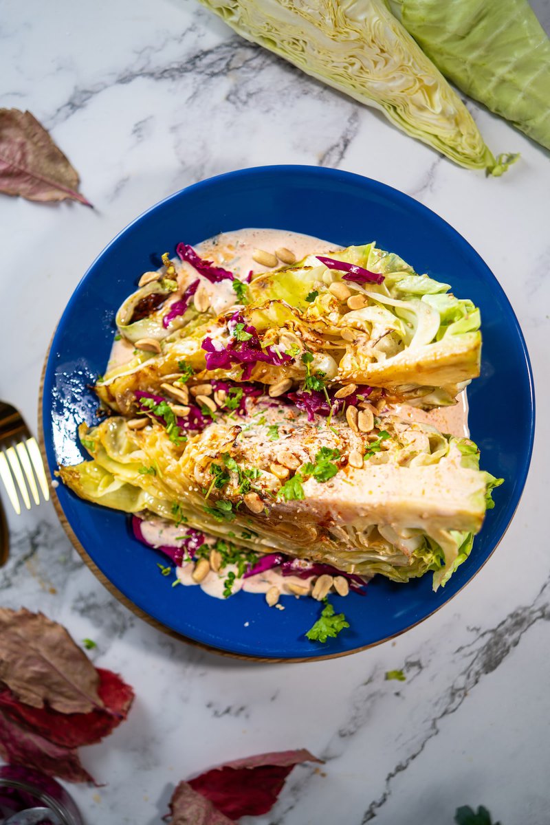 Overhead view of charred cabbage steaks with spicy aioli, toasted nuts and red cabbage slaw on cobalt blue plate