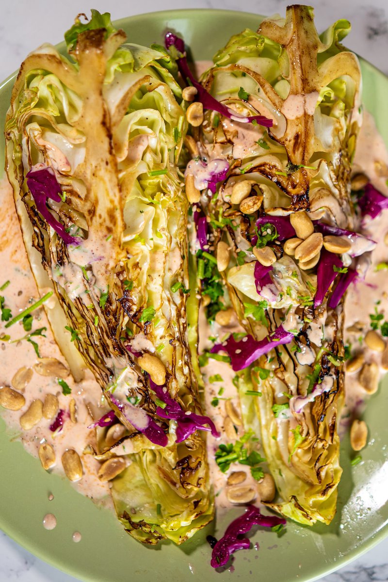 Close-up of grilled cabbage quarters with charred edges, creamy dressing, purple cabbage slaw and crushed peanuts on mint green plate