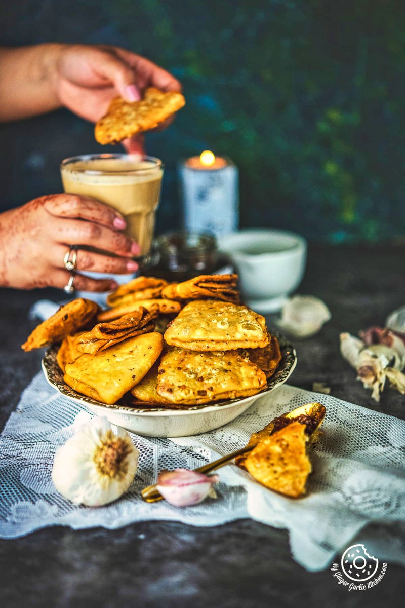 Image of a female holding Cheese Garlic Masala Mathri over a chutney jar