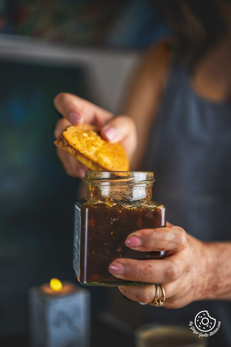 Image of a female holding Cheese Garlic Masala Mathri over a chutney jar