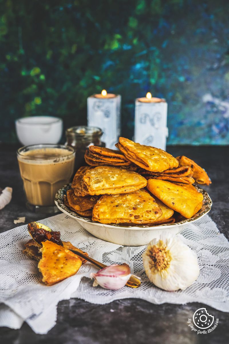 Image of Cheese Garlic Masala Mathri serevd in a bowl along with a cup of coffee and candles in background