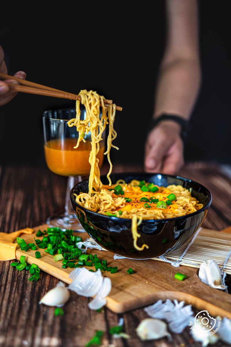 photo of a person holding chopsticks over a bowl of cheese ramen noodles
