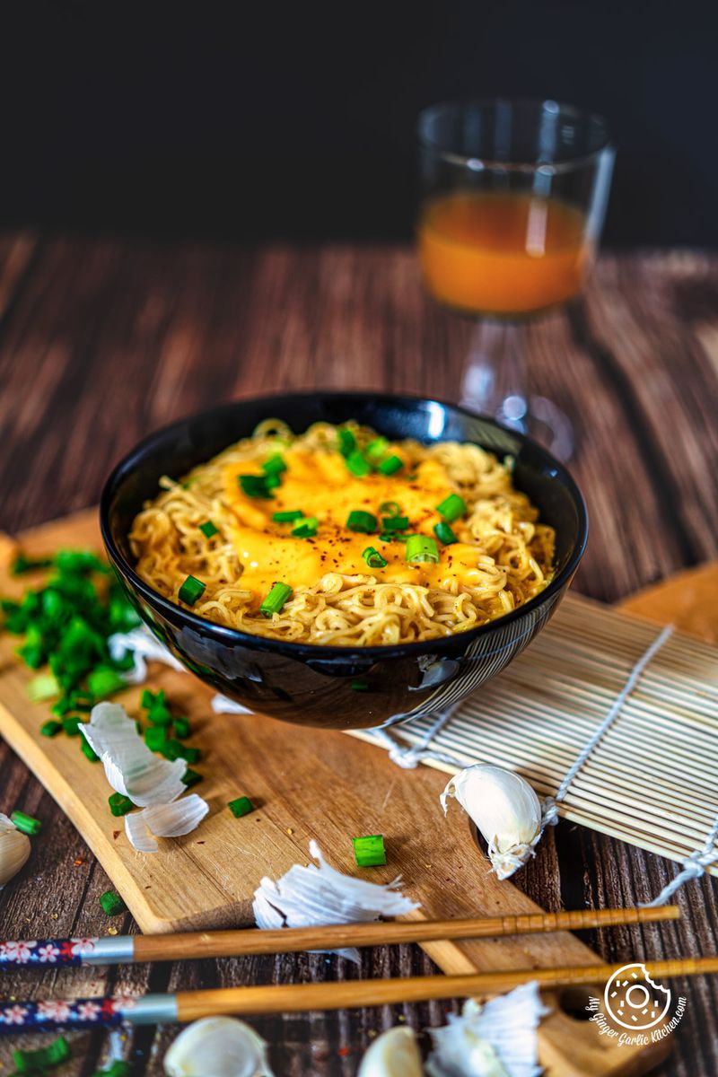 photo of a bowl of cheese ramen with green onions and garlic on a wooden board