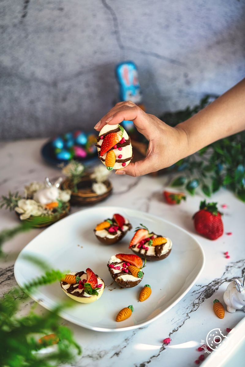 a hand holding a cheesecake filled easter egg over a white plate with cheesecake filled easter eggs