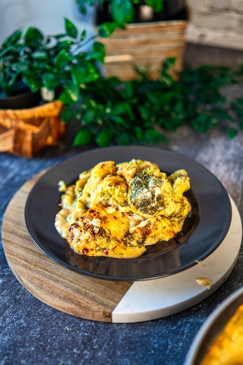 Cheesy broccoli casserole with creamy garlic cheese sauce and golden melted Emmental cheese, served on a black plate