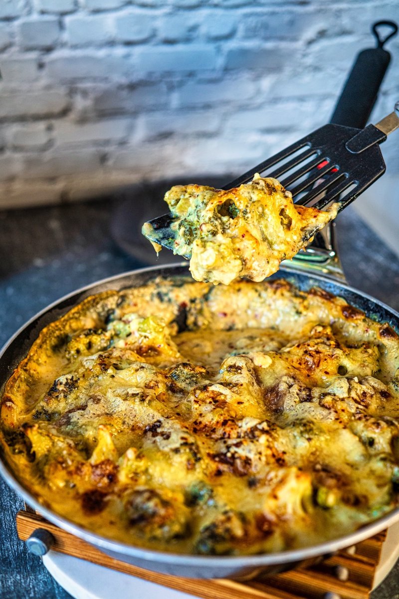 Cheesy broccoli casserole with golden melted cheese, creamy sauce, and tender broccoli lifted from the skillet on a spatula