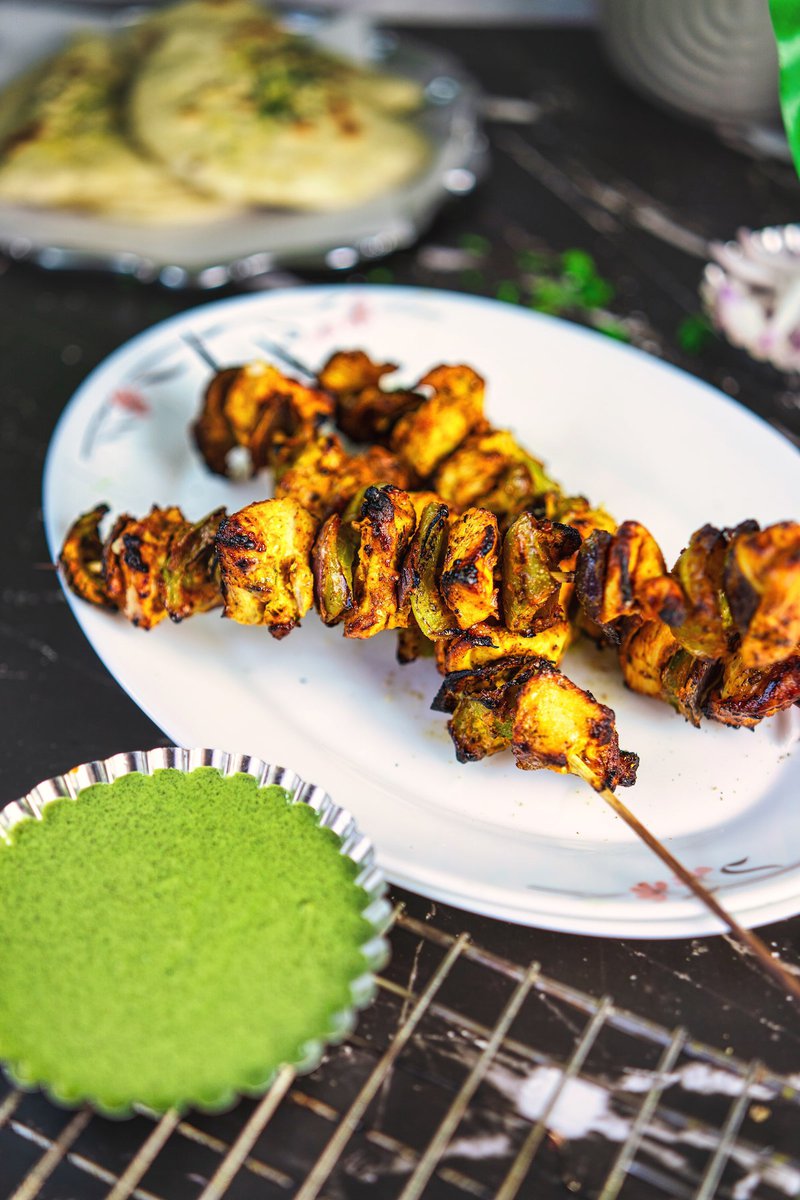 Succulent chicken tikka pieces cooked to perfection, served on a plate alongside vibrant mint chutney for a burst of flavor.