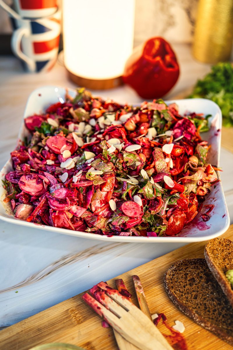 Vibrant and colorful beetroot chickpea salad on a plate with wooden utensils and a red bell pepper in the background.