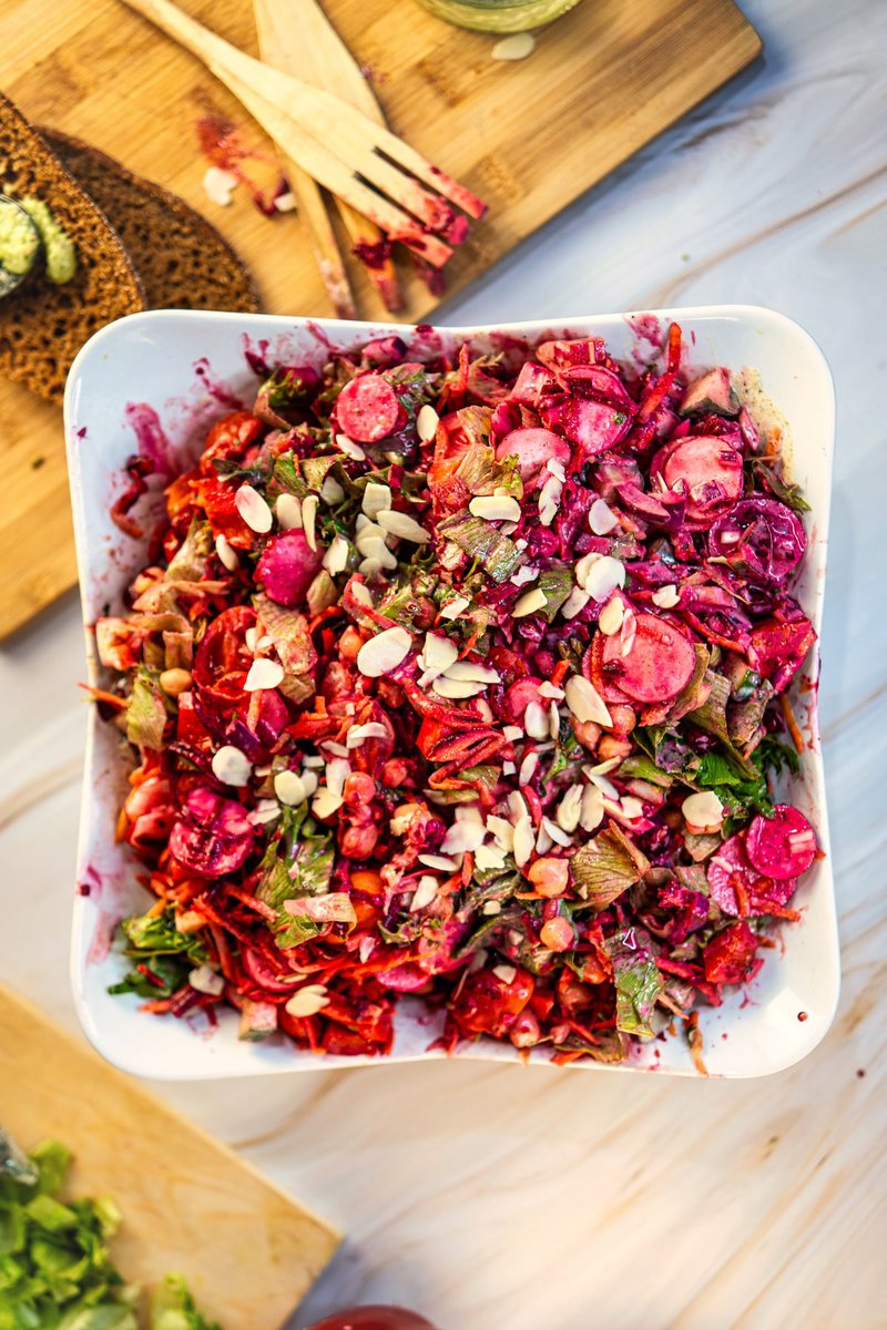 Freshly prepared beetroot and chickpea salad in a white dish, with wooden utensils and a red bell pepper visible