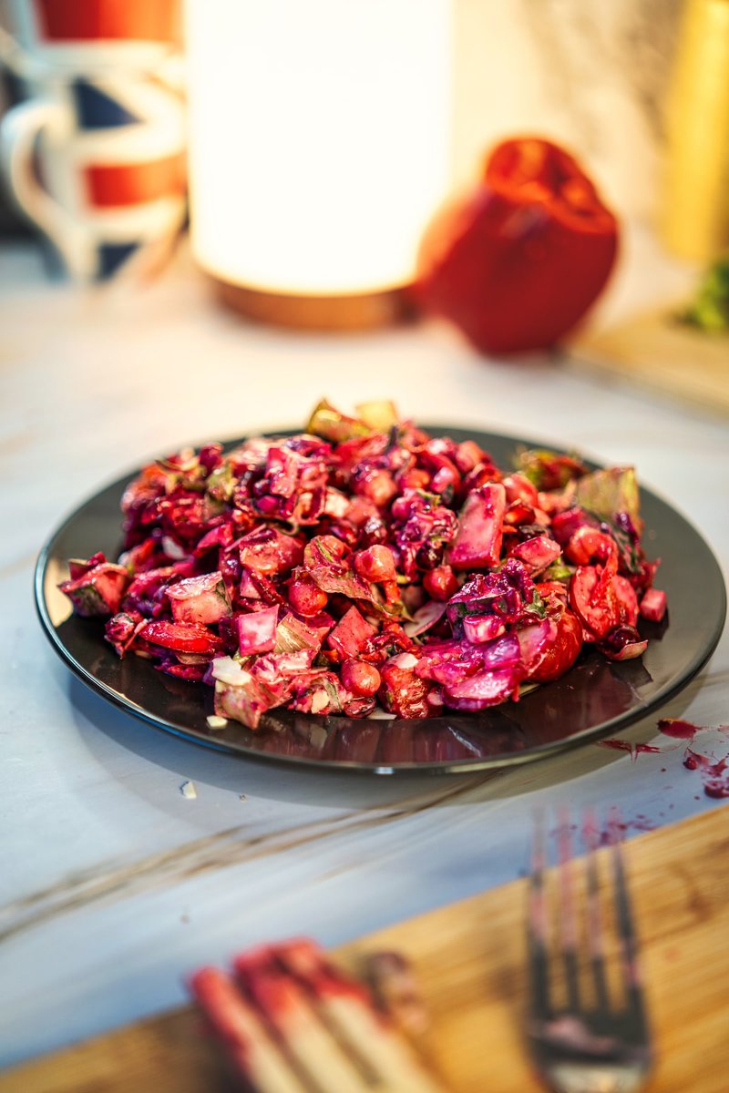 Appetizing chickpea beetroot salad dish in a dark plate, with a red bell pepper and wooden utensils visible in the background.