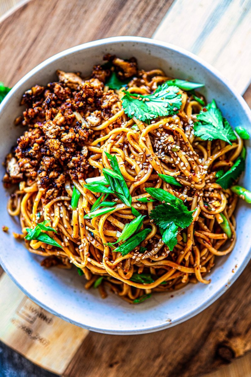 Chili Garlic Noodles with crispy tofu crumbles, sesame seeds, cilantro, and spring onions served in a bowl