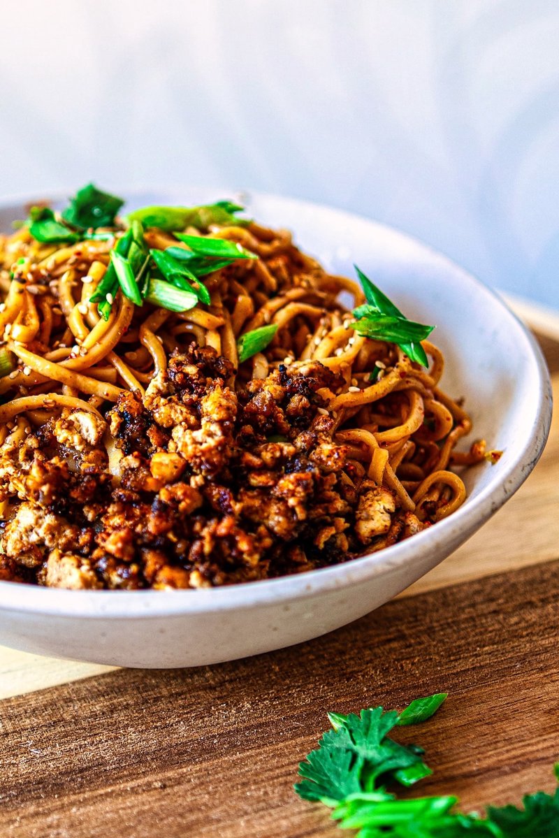 Close-up of Chili Garlic Noodles topped with crispy tofu crumbles, spring onions, and sesame seeds