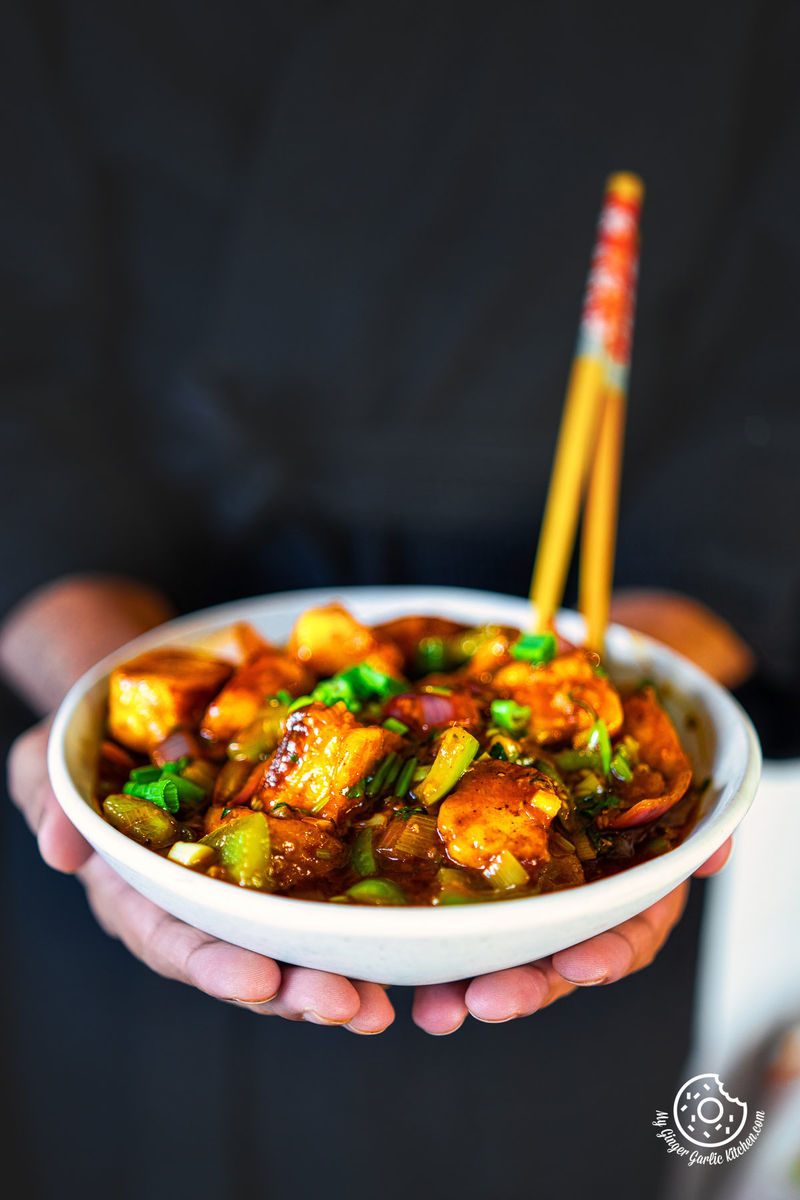 photo of a person holding a bowl of paneer chilli with chopsticks