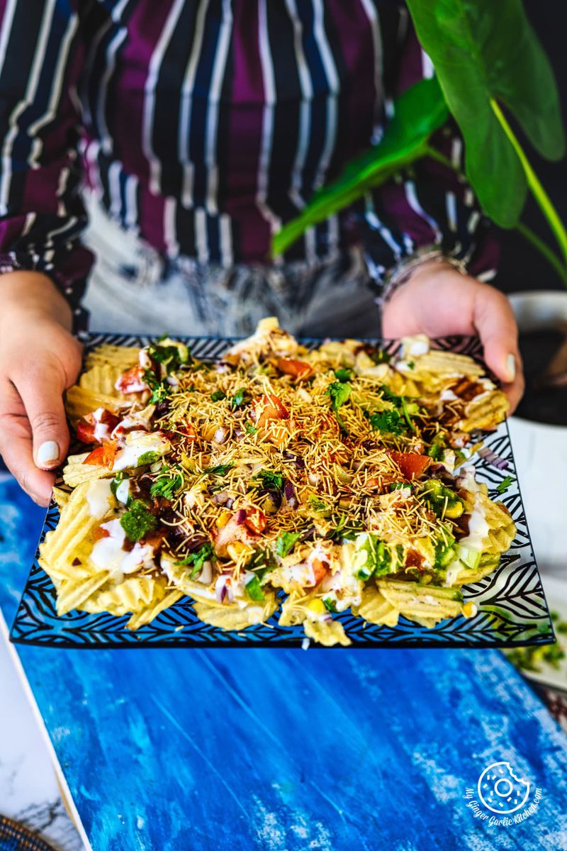 a feamle holding chips chaat kept in a square plate