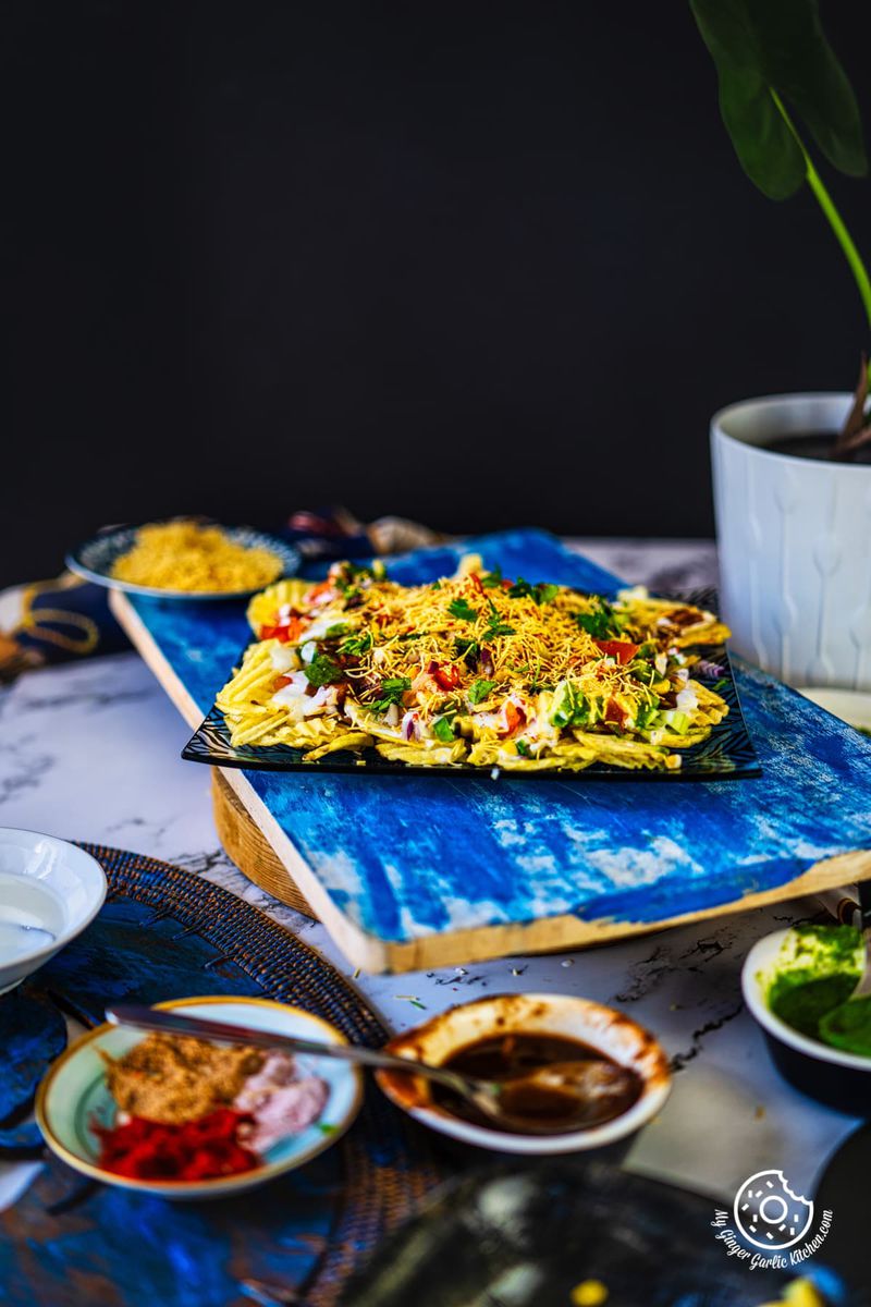 chips chaat plate kept on a blue wooden board and chutnys on the side