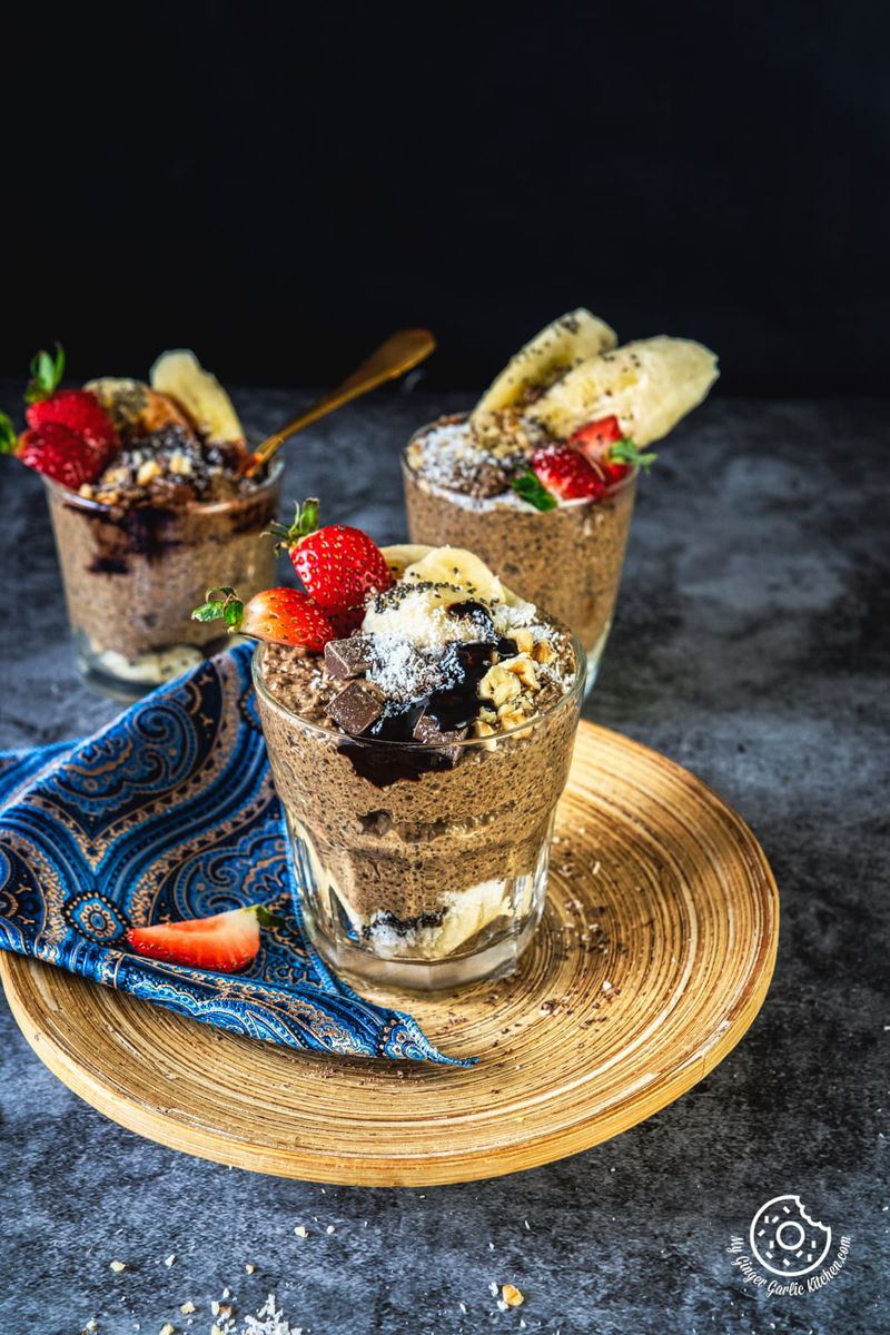 chocolate coffee chia pudding glass topped with chocolate and coconut kept on a wooden plate and two pudding glasses in the background