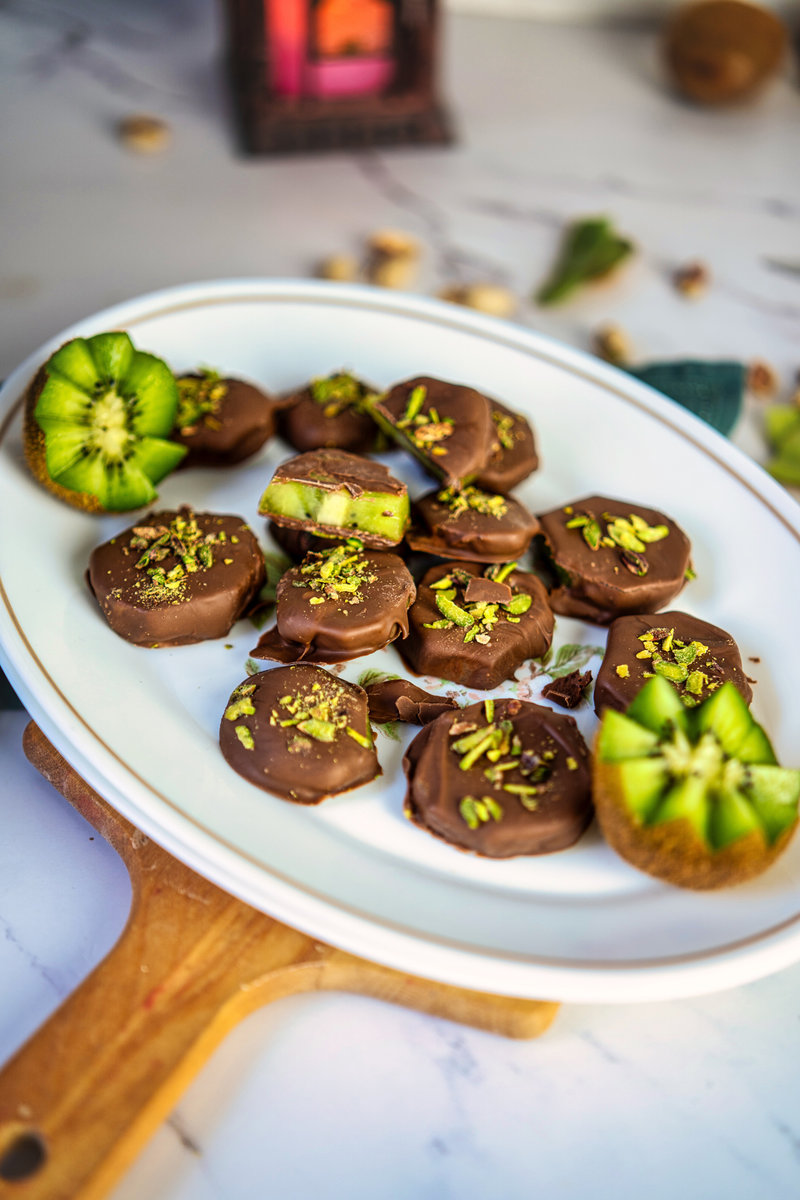 a white plate of chocolate covered kiwis on a table