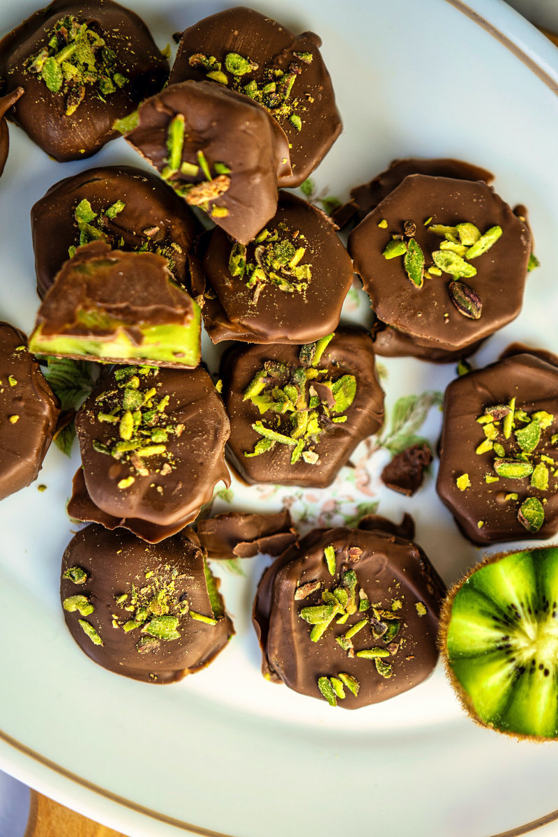 close up of chocolate dipped kiwi desserts and kiwi fruit on a plate