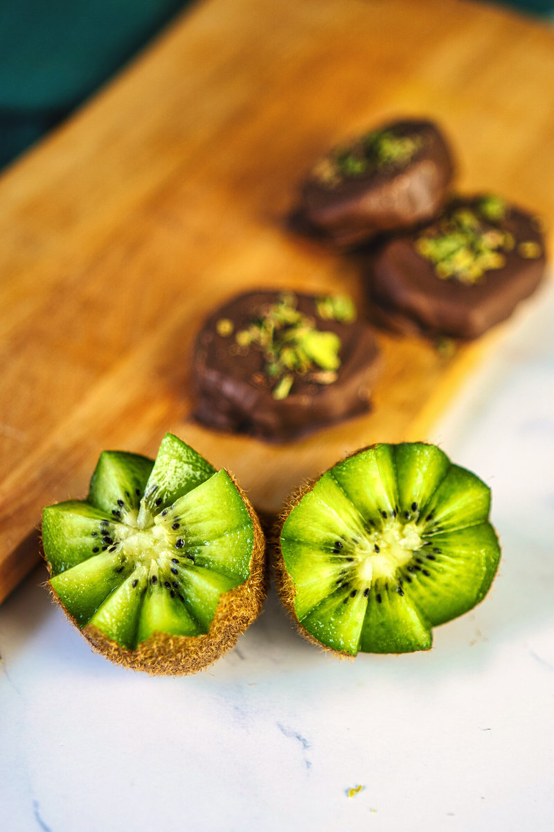 two pieces of kiwi with three pieces of chocolate covered kiwis on a cutting board