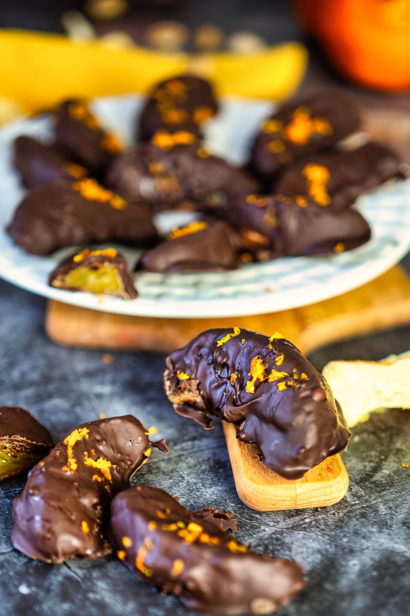 chocolate covered orange slice on a wooden board with some more chocolate coated oranges on a plate