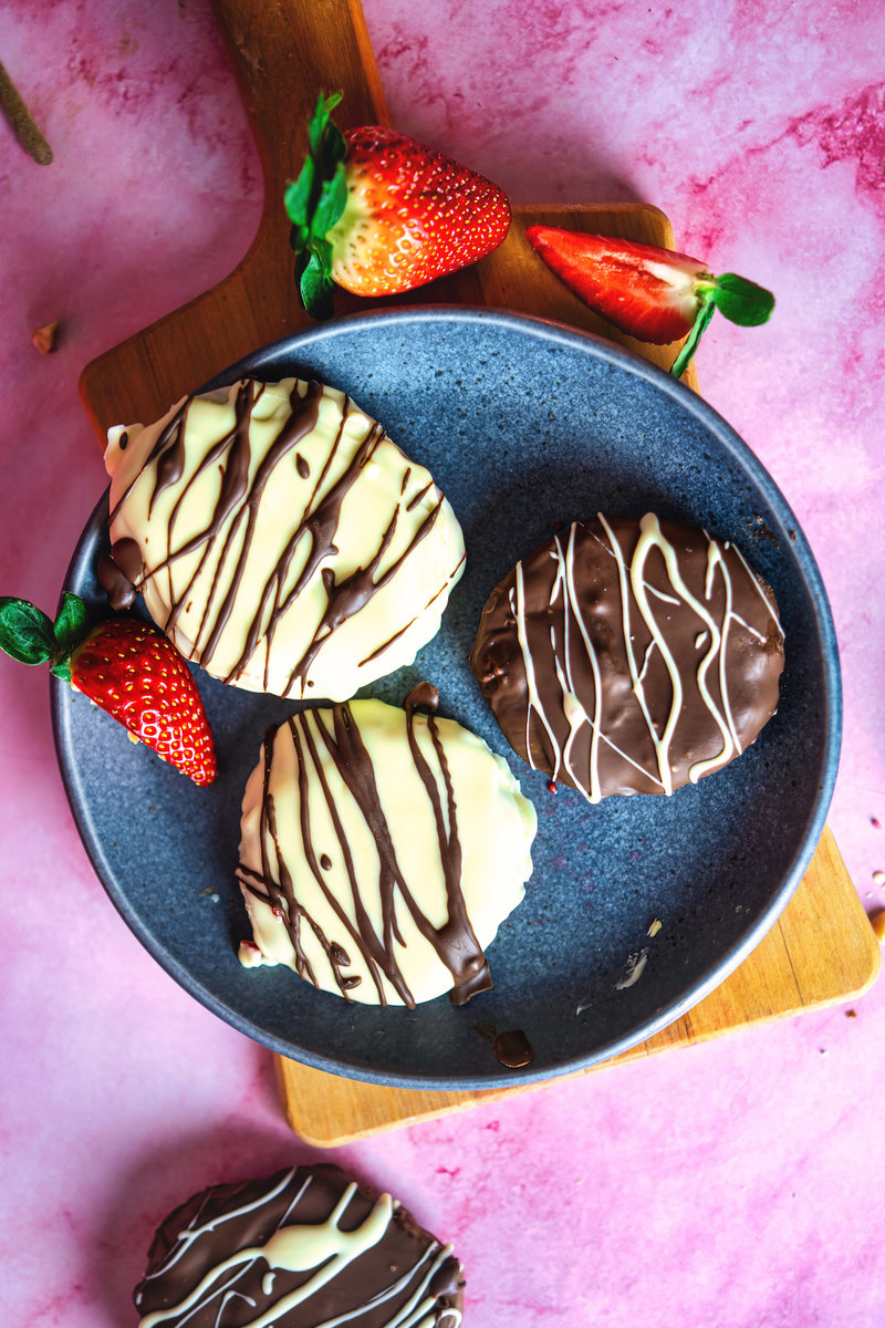Overhead view of chocolate covered raspberry bites with white and dark chocolate drizzle on a plate, accompanied by fresh strawberries