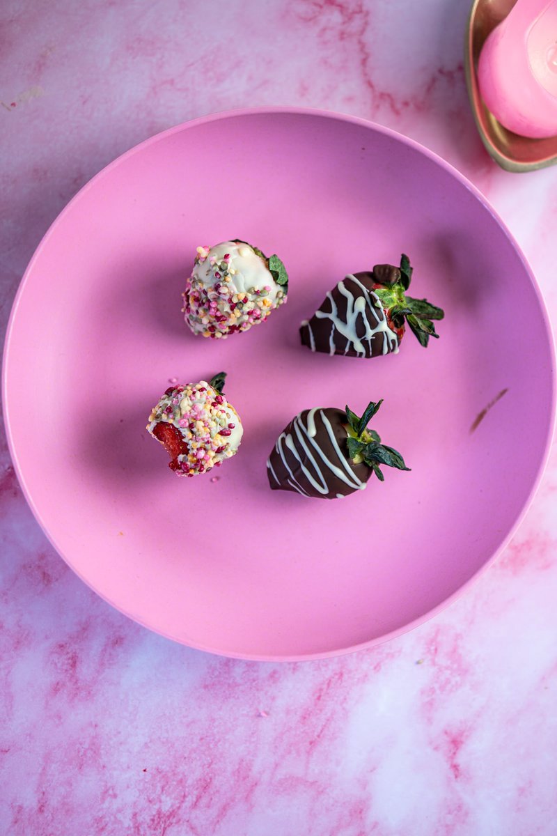 Few chocolate coated strawberries on a pink plate with a pink marbled background