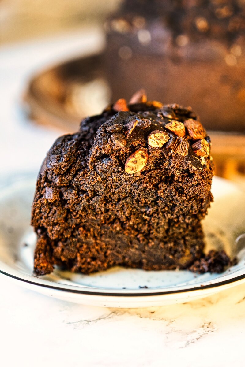 Moist eggless chocolate date cake on rustic plate, topped with chopped almonds and chocolate chips, refined-sugar-free vegan dessert recipe