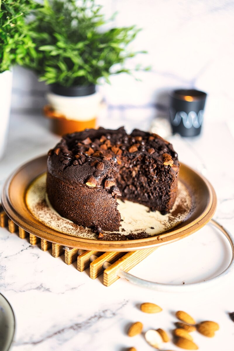 Close-up of thick slice from chocolate date cake showing dense fudgy crumb, studded with almond pieces and chocolate chips, dairy-free festive treat