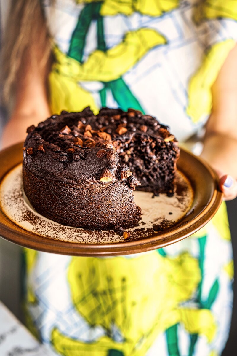 Partially sliced chocolate date cake on plate, rich moist interior with almond topping and dark chocolate chips, simple eggless bake for celebrations