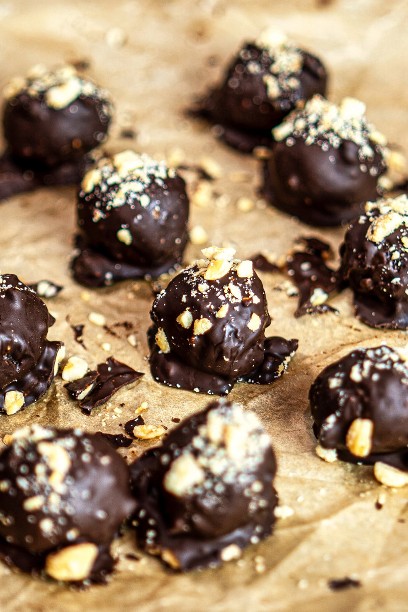 Close-up of chocolate hazelnut bliss balls sprinkled with chopped nuts on parchment paper.