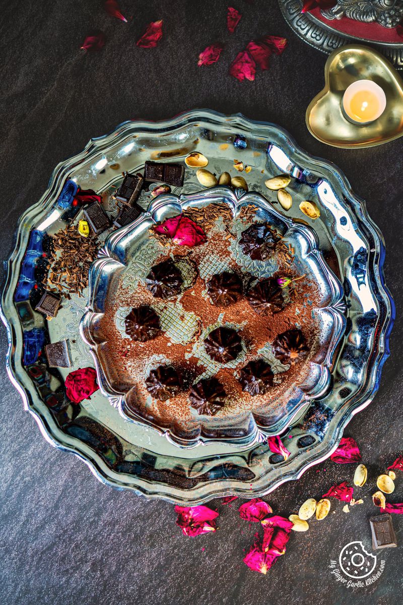 overhead shot of 9 chocolate modaks in a steel plate with a candle on the side