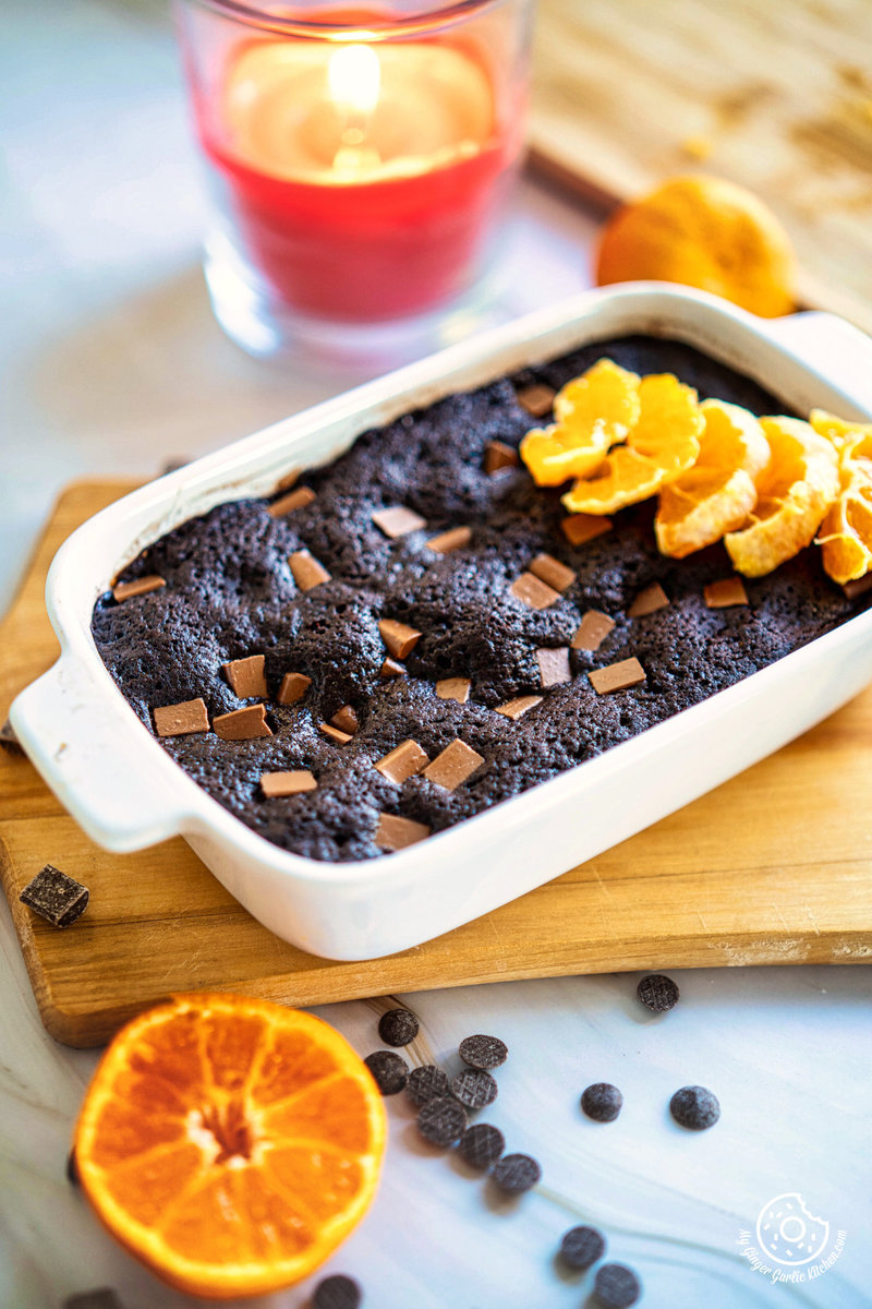 a chocolate orange mug cake with a piece taken out in a white dish with orange slices