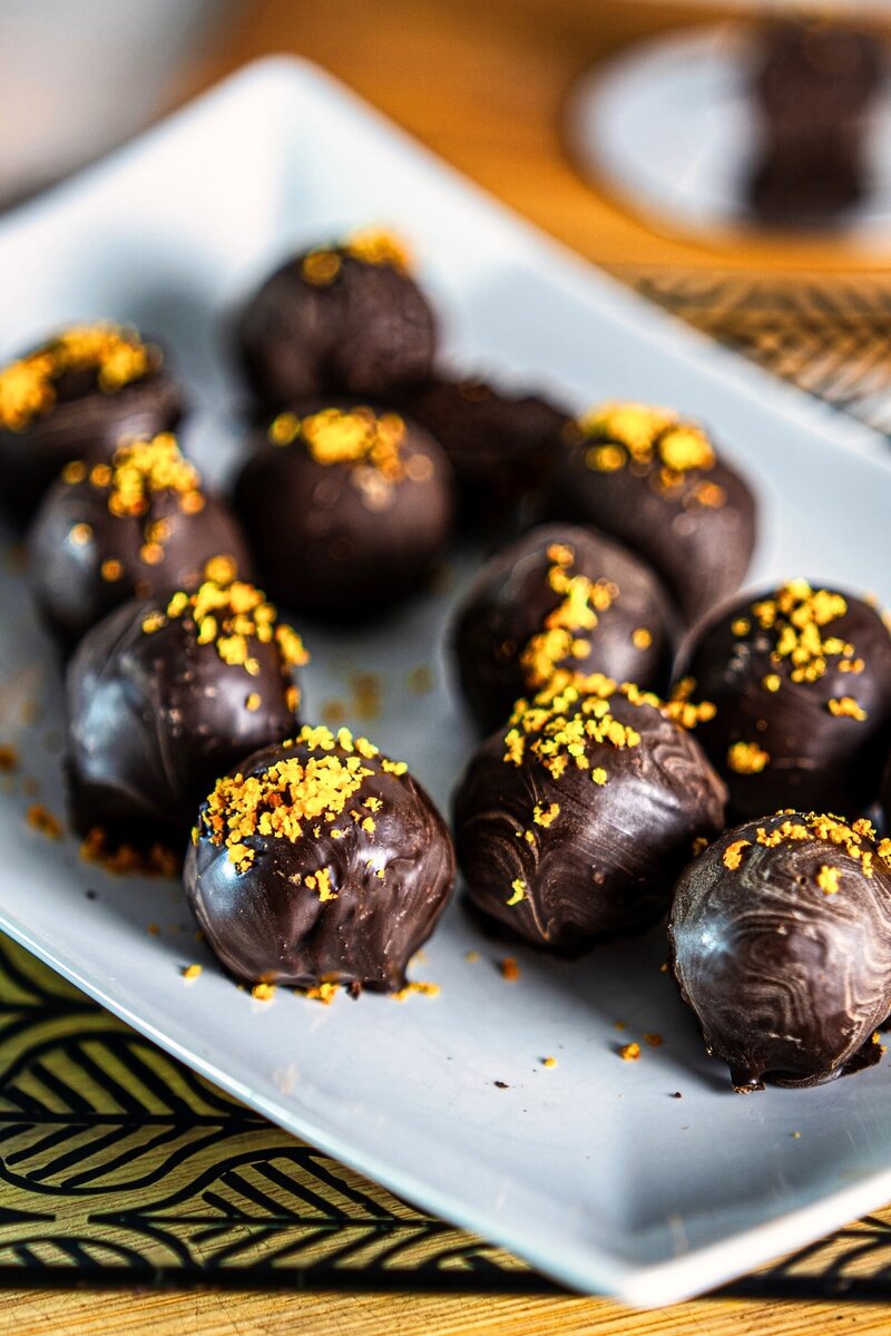 Vegan chocolate orange truffles coated in dark chocolate and topped with fresh orange zest on a white plate