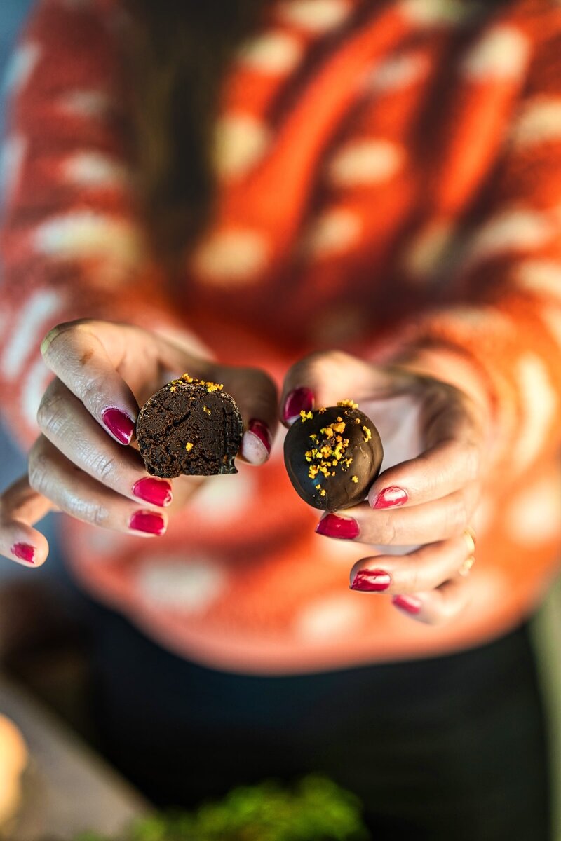 Hands holding vegan chocolate orange truffles, one cut open to show creamy chocolate orange ganache center
