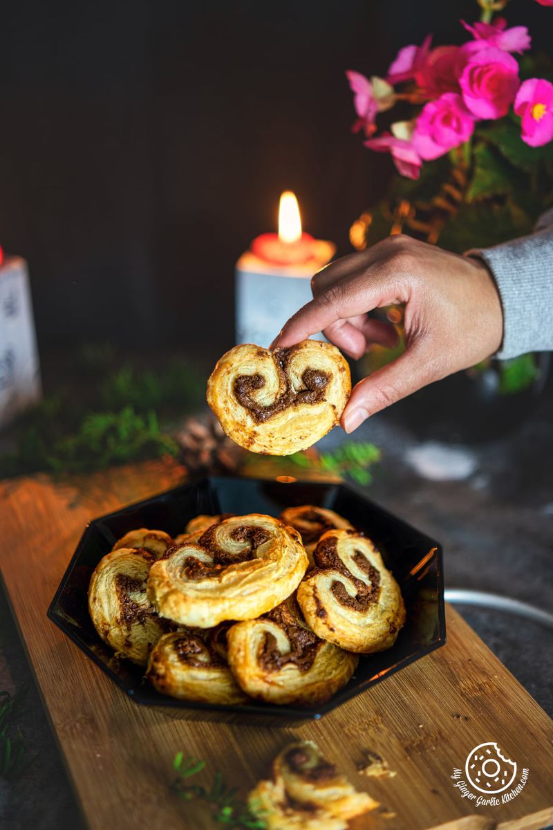 chocolate palmiers in a black plate with a person holding one chocolate palmier