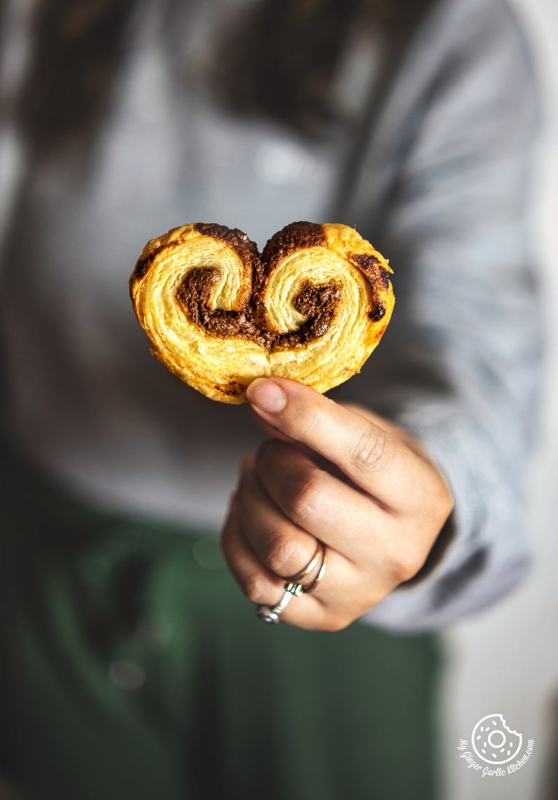 a hand holding one chocolate palmier over black plate with chocolate palmiers